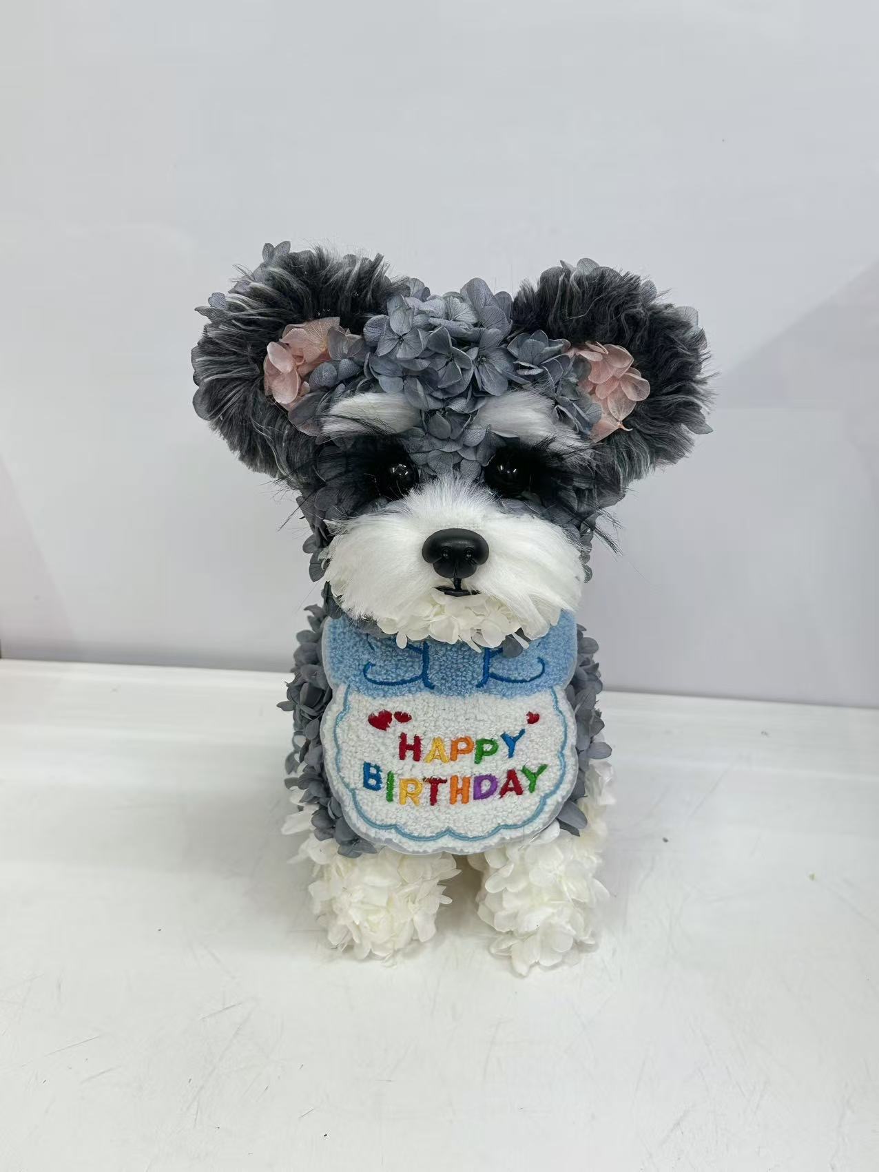 グレーと白の花びらで形づくられ、バースデーの小物を身につけた犬の作品