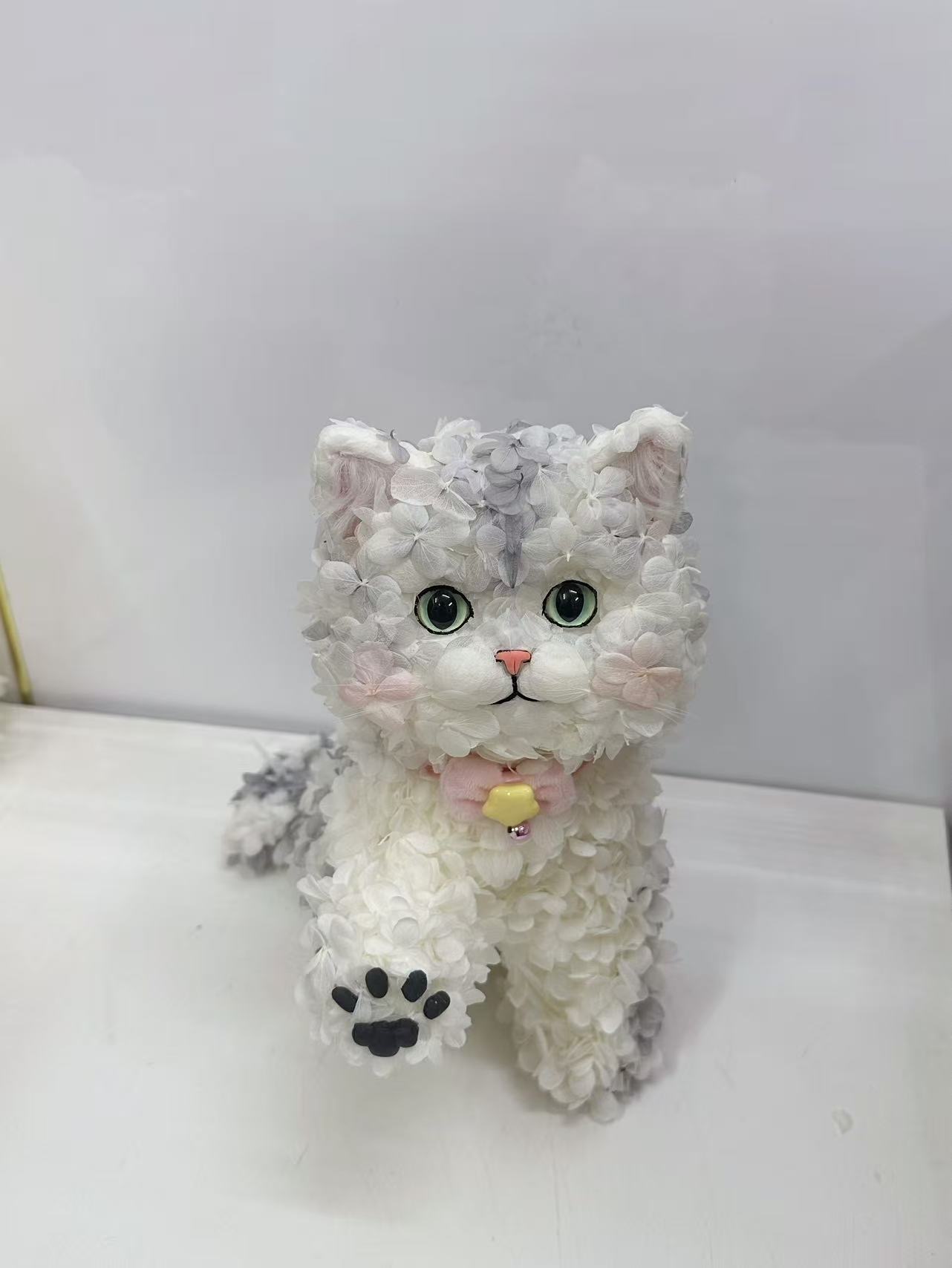 白と淡いグレーの花びらで形づくられ、前足の肉球を見せる猫の作品